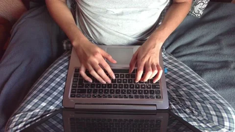 Overhead view of a young man in striped pajamas with a laptop on his legs typing Stock Footage 156259430