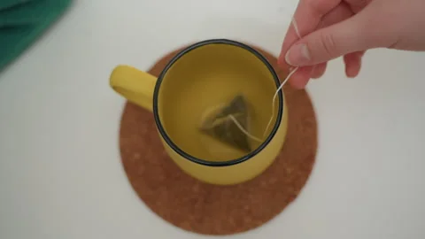 Overhead yellow mug with hand dropping teabag into cup fingers adjust string Stock Footage 337229599