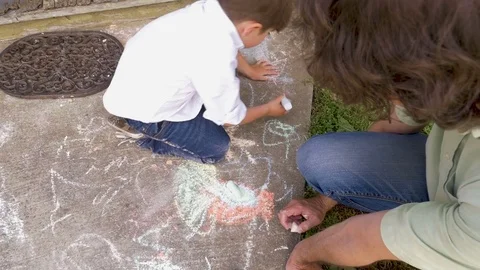 Overhead of a young boy drawing with chalk using both hands with his father Stock Footage 83146114