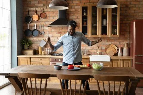 Overjoyed afro american guy dance by kitchen table preparing meal Stock Photos