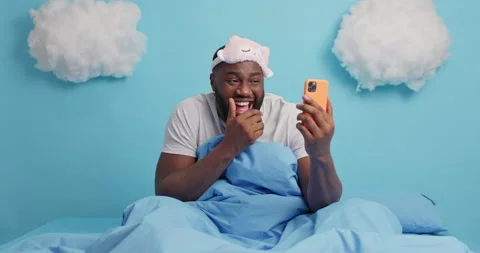 Overjoyed black man laughs positively keeps smartphone in front has video Stock Footage 148993192