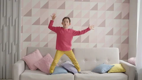 Overjoyed cute active boy jumping on sofa in cozy living room, charming happy Stock Footage 153836333