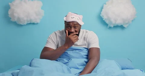 Overjoyed dark skinned bearded man poses in comfortable bed laughs out hears Stock Footage 148990944
