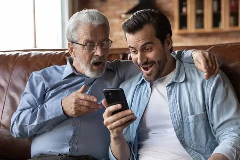 Overjoyed surprised two generations of men looking at phone screen Stock Photos