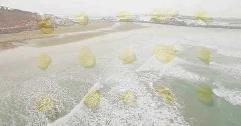 Overlaying yellow circle pattern on sandy beach at snow-dusted cliffs with ocean Stock Photos