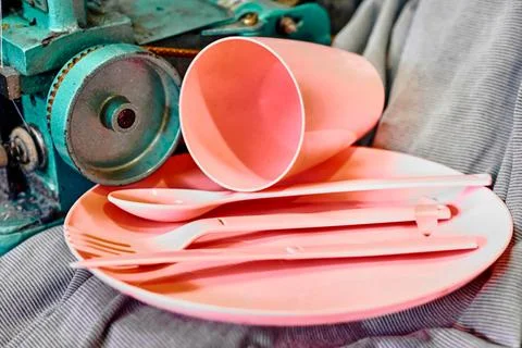 Overlock.Pink plastic dinnerware set in tailor workshop.Cup,fork,knife,spoon Stock Photos