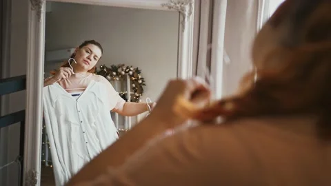 Oversize lady choosing blouse in dressing room, looking at mirror, plus size Vidéo 143566872