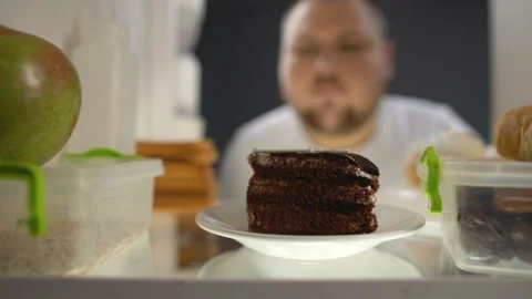 Oversize man taking piece of cake from fridge at night, diabetes risk, calories Stock Footage 89448529