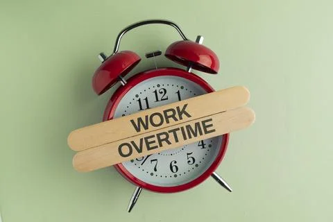 OVERTIME PAY text on a white card placed on a red vintage alarm clock over .. 库存照片
