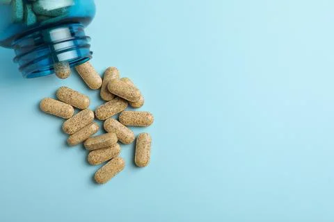 Overturned bottle with dietary supplement pills on light blue background, fla Stock Photos