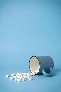 Overturned cup with marshmallows on a blue background. Cocoa drink concept Stock Photos