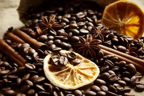 Overturned sack full of coffee beans, dried oranges,anises and cinnamon on bl Stock Photos