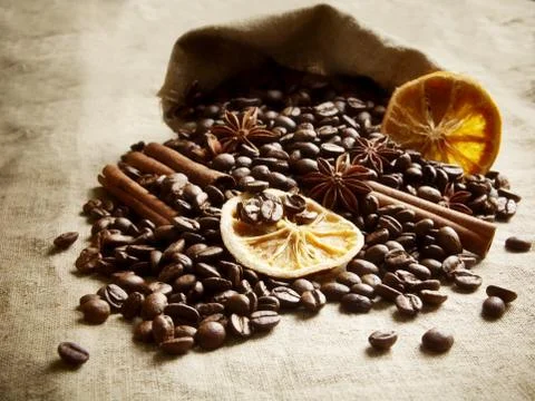 Overturned sack full of coffee beans, dried oranges,anises and cinnamon on bl Stock Photos