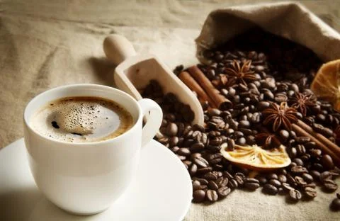 Overturned sack full of coffee beans with coffee cup, dried oranges,anises an Stock Photos