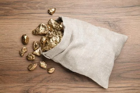 Overturned sack of gold nuggets on wooden table, flat lay Stock Photos