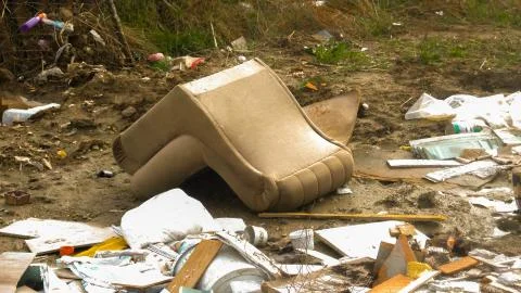An overturned sofa in a landfill surrounded by garbage Stock Photos