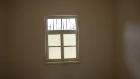 Overview of a bare room with a barred window, wooden floor and round lamp Stock Footage 299043984