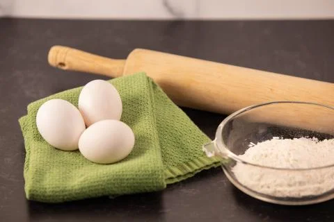 Overview of three eggs sitting on dish towel wooden rolling pin and flour Stock Photos