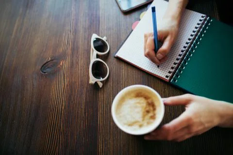 Overview of woman's hands writing in a notepad, holding coffee. Stock Photos