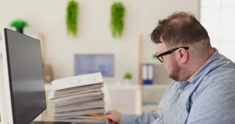 Overweight accountant reviewing paperwork at computer in office, finance tasks Stock Footage 334710549