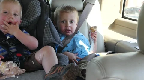 Overweight child eating tipped over ice cream in his car seat. Stock Footage