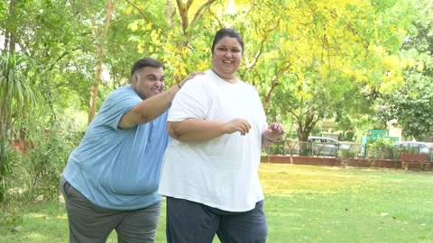 Overweight couple having fun together at summer park. Fat man pushing woman.. Stock Footage 312908195