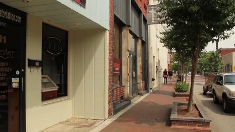 Overweight Couple walks down a Small Downtown Sidewalk Stock Footage 83058248