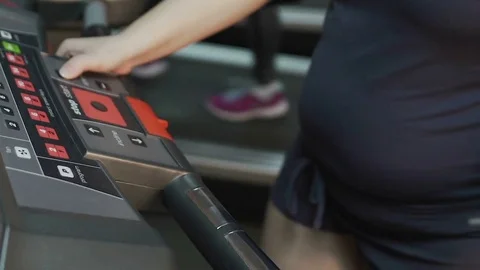 Overweight female walking on treadmill, setting up speed on panel, exercising Video stock 76970928