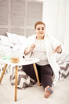 Overweight ginger lady checking her manicure while sitting on bed Stock Photos