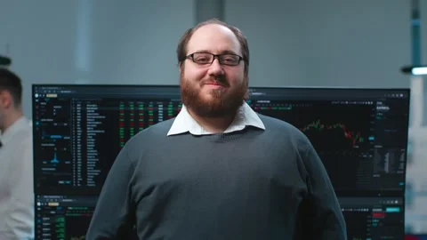 Overweight it-programmer smiling at camera with multiple screens with charts on Stock Footage 244860073