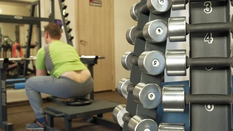 The overweight man does squats with squats with a weight disc for a barbell Video stock 107507272
