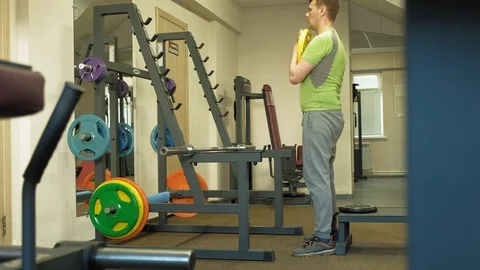 The overweight man does squats with squats with a weight disc for a barbell Video stock 107507300
