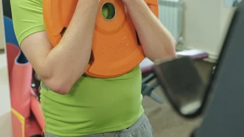The overweight man does squats with squats with a weight disc for a barbell Video stock 108135336