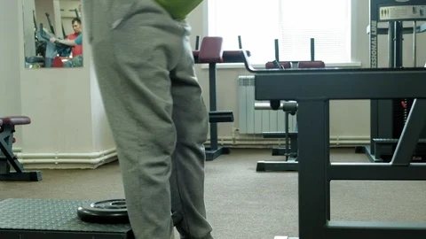 The overweight man does squats with squats with a weight disc for a barbell Video stock 108135681