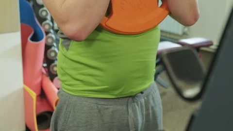 The overweight man does squats with squats with a weight disc for a barbell Video stock 108135765