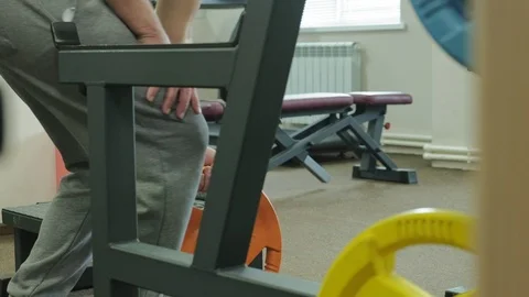 The overweight man does squats with squats with a weight disc for a barbell Video stock 108135792