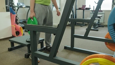 The overweight man does squats with squats with a weight disc for a barbell Video stock 108136251