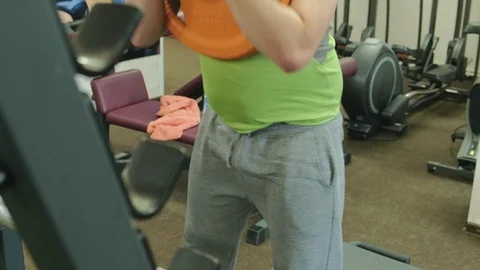 The overweight man does squats with squats with a weight disc for a barbell Video stock 108136461