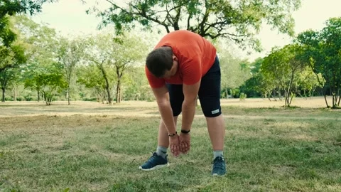 An overweight man does a warm-up, bends forward, before training in the park Stock Footage 138820606