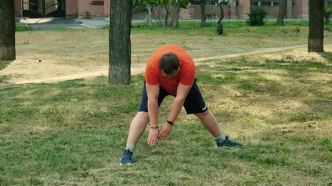 An overweight man does a warm-up, bends forward, before training in the park Stock Footage 138821034