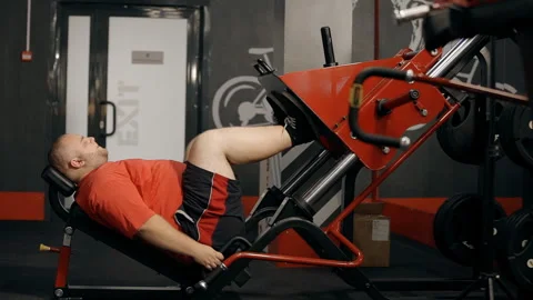 Overweight man doing exercise on leg press trainer at the gym. working out to Stock Footage 119395807