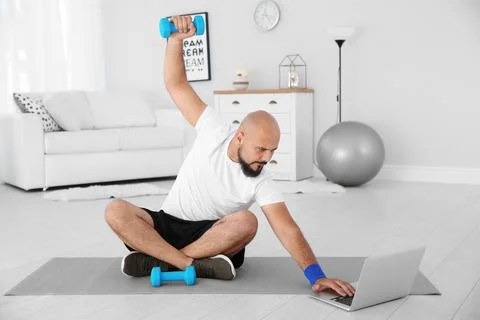 Overweight man doing exercise while watching tutorial on laptop at home Foto stock