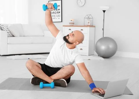 Overweight man doing exercise while watching tutorial on laptop at home 스톡 사진