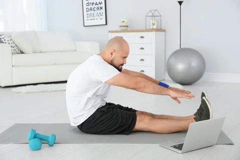 Overweight man doing exercise while watching tutorial on laptop at home Foto stock