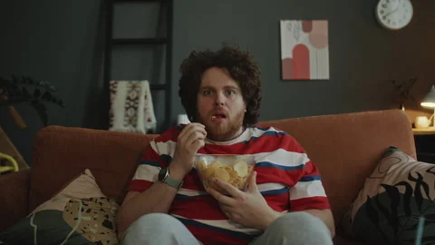 Overweight Man Eating Chips and Getting Scared as Watching Horror on TV Stock Footage 303208449
