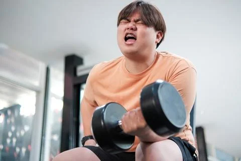 Overweight man grimacing while lifting dumbbell Foto stock