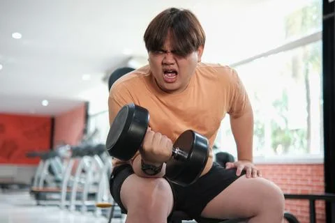 Overweight man grimacing while lifting dumbbell Stock Photos