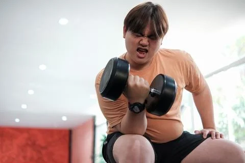 Overweight man grimacing while lifting dumbbell Foto stock