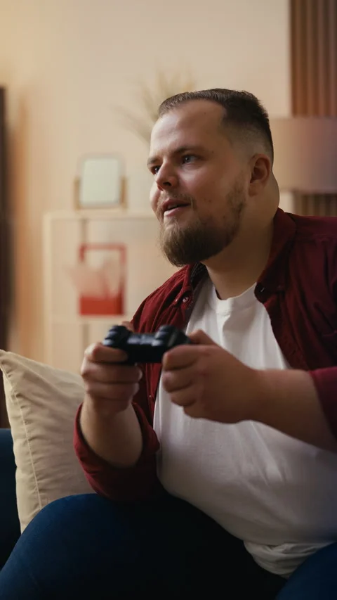 Overweight man sitting on the couch at home, playing video games with a gamepad Video stock 306372974