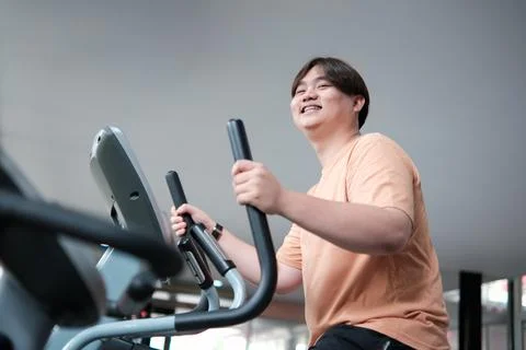 Overweight man smiling while exercising on elliptical Stock Photos